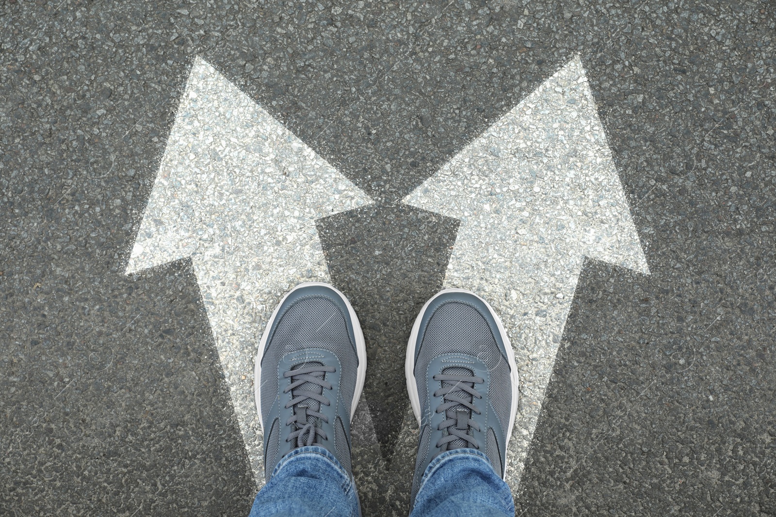 Image of Man standing on asphalt road with white arrows pointing in different directions, top view. Concept of choice and making decisions