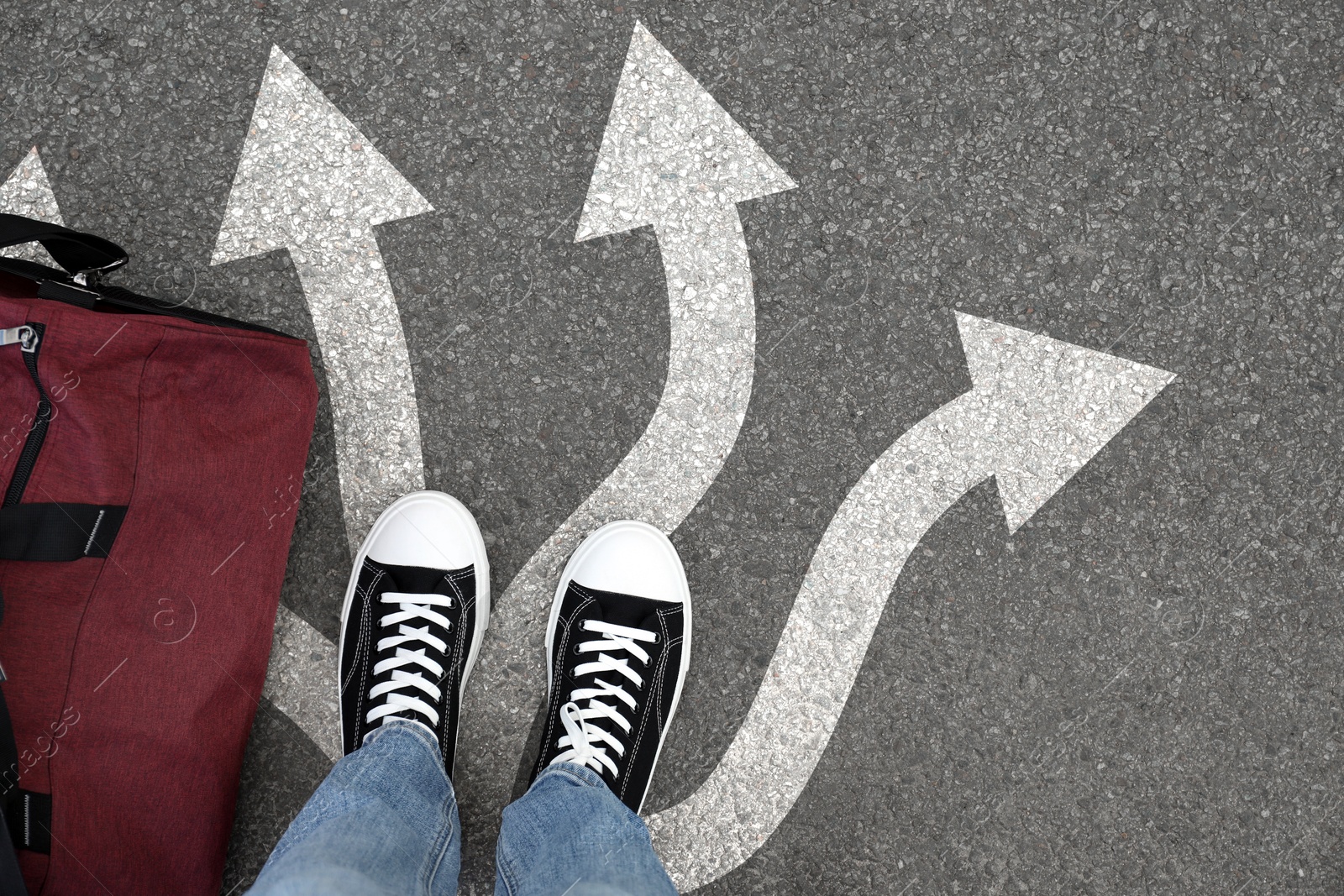 Image of Man standing on asphalt road with white arrows pointing in different directions, top view. Concept of choice and making decisions