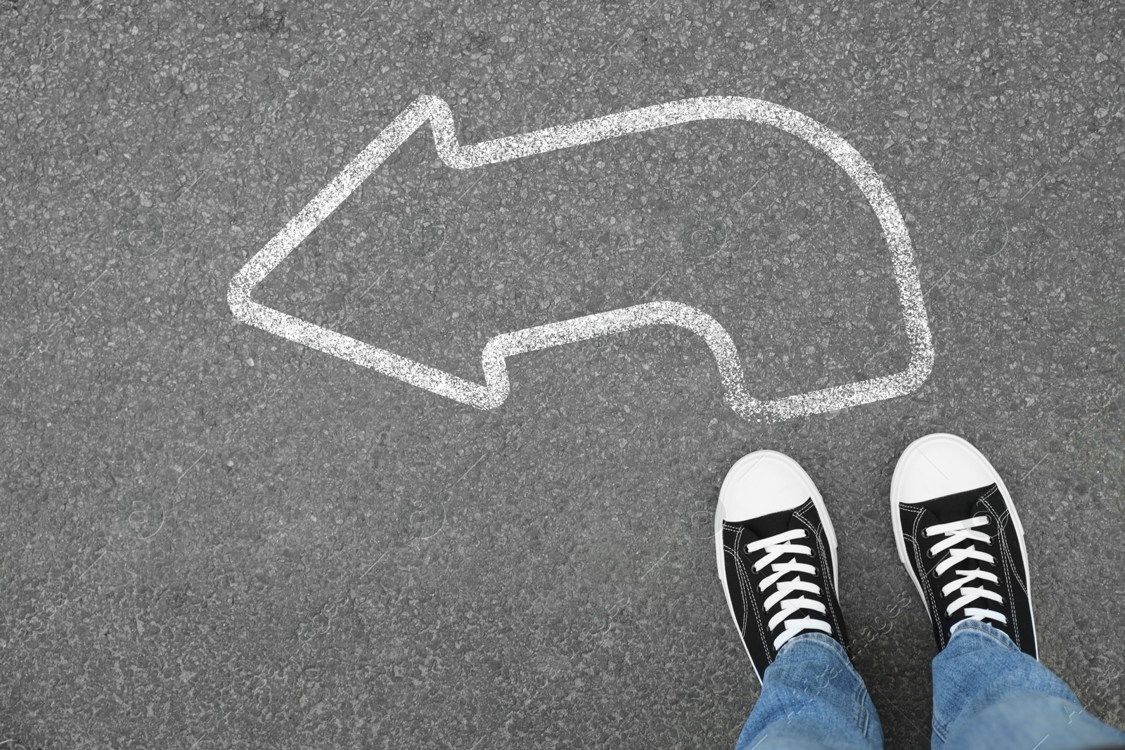 Image of Man standing on asphalt road with white arrow, top view