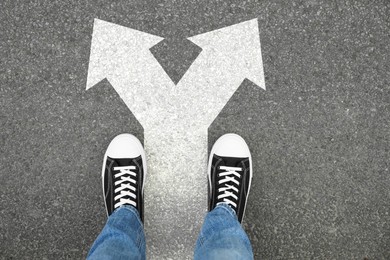 Image of Man standing on asphalt road with white arrows pointing in different directions, top view. Concept of choice and making decisions