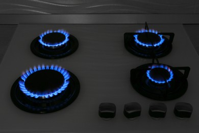 Photo of Modern gas cooktop with burning blue flames in kitchen at night