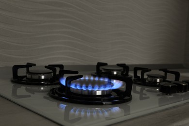 Photo of Modern gas cooktop with burning blue flame in kitchen