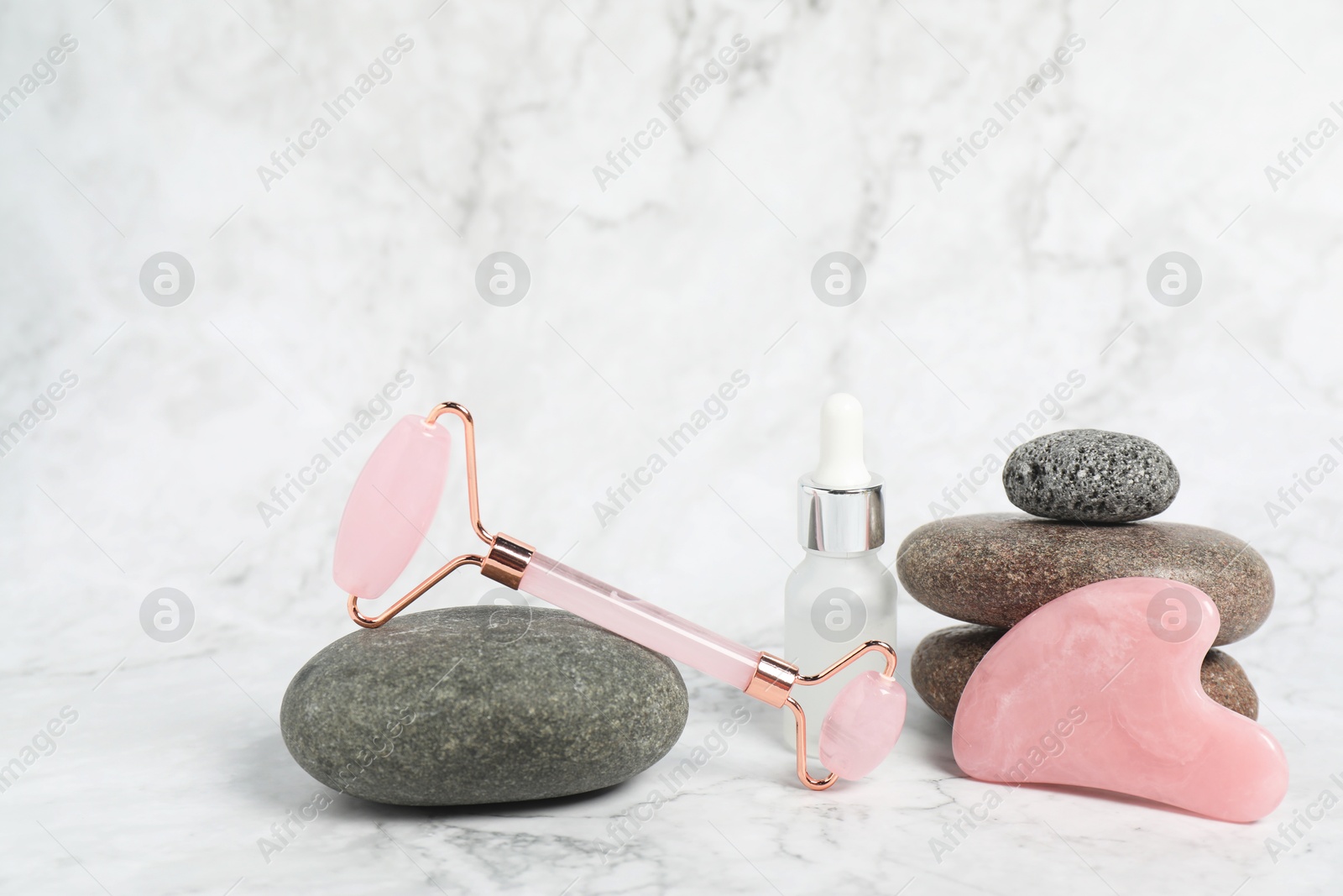 Photo of Face roller, gua sha tool, cosmetic product and stones on white marble background. Space for text