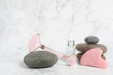 Photo of Face roller, gua sha tool, cosmetic product and stones on white marble background. Space for text