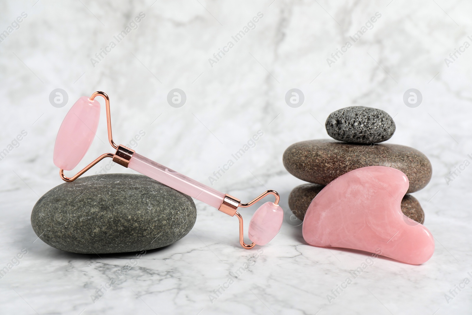 Photo of Face roller, gua sha tool and stones on white marble background