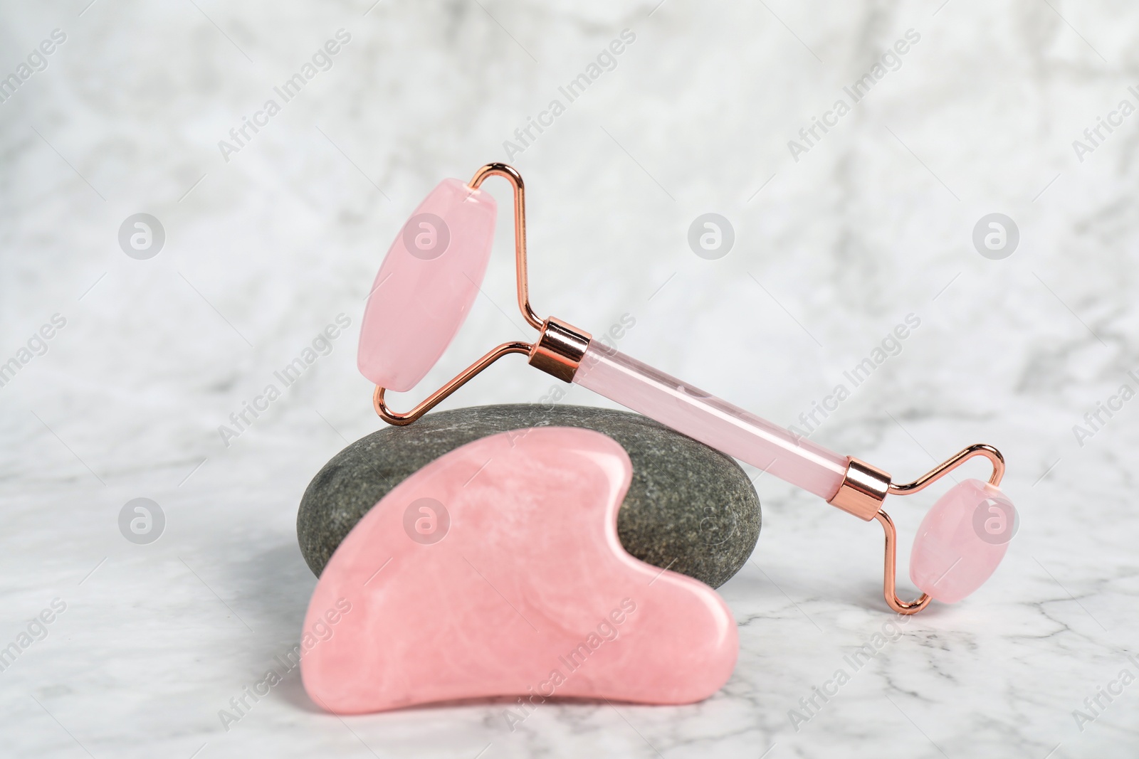 Photo of Face roller, gua sha tool and stone on white marble background