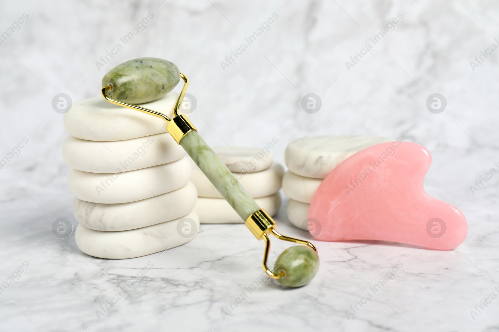 Photo of Face roller, gua sha tool and massage stones on white marble background