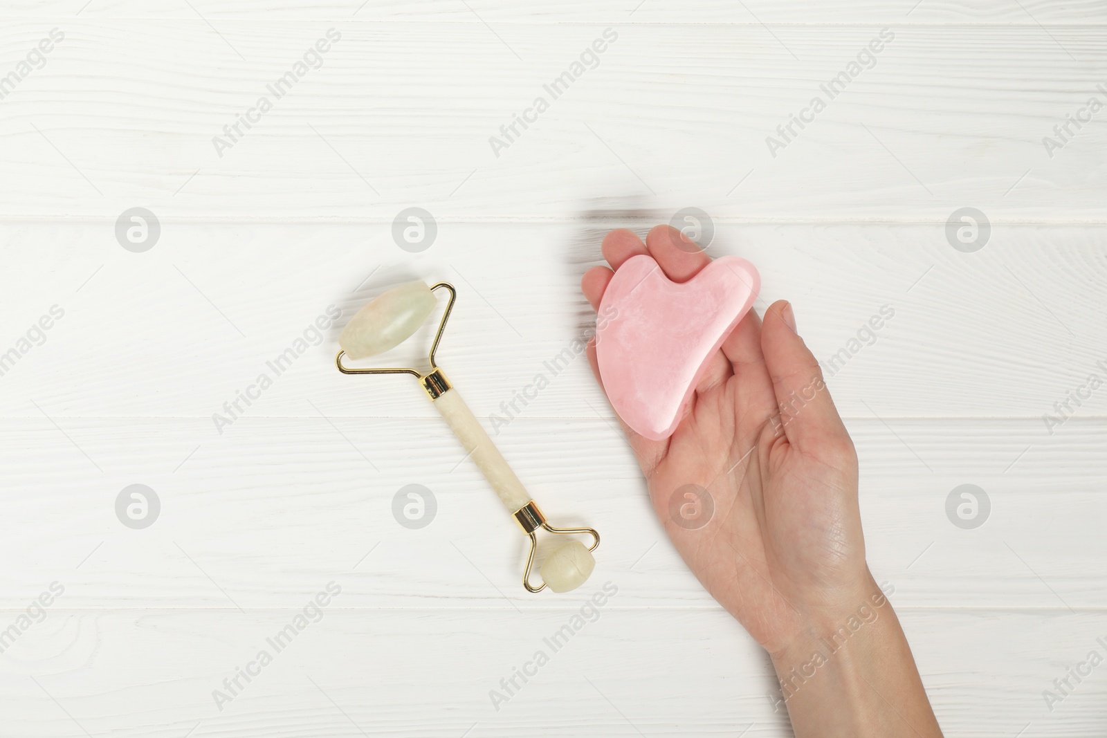 Photo of Woman with face roller and gua sha tool on white wooden background, top view