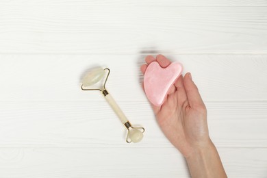 Photo of Woman with face roller and gua sha tool on white wooden background, top view