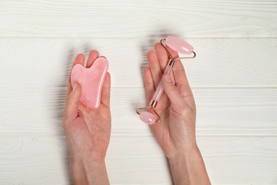 Photo of Woman with face roller and gua sha tool on white wooden background, top view