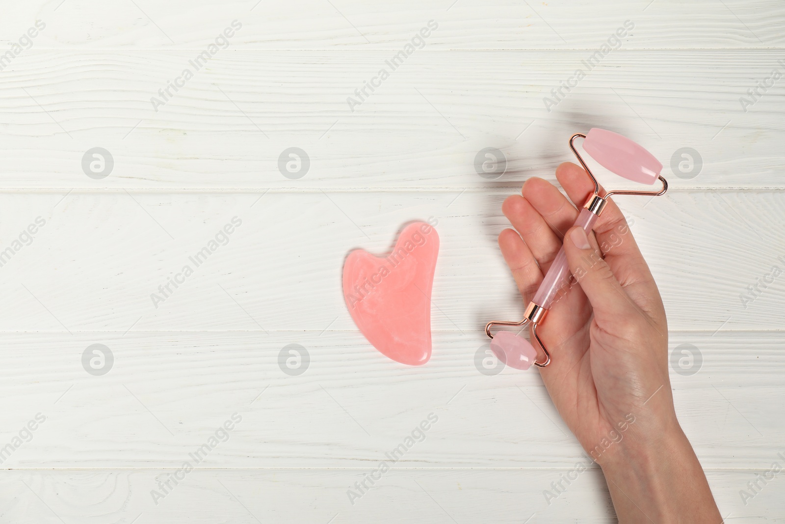 Photo of Woman with face roller and gua sha tool on white wooden background, top view. Space for text