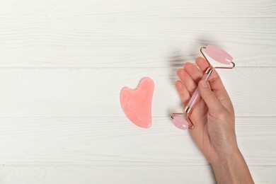 Photo of Woman with face roller and gua sha tool on white wooden background, top view. Space for text