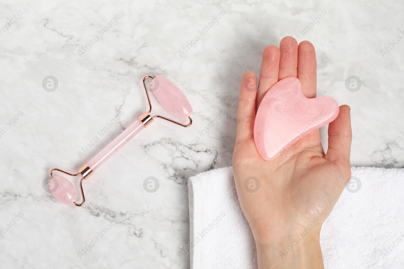 Photo of Woman with face roller and gua sha tool on white marble background, top view