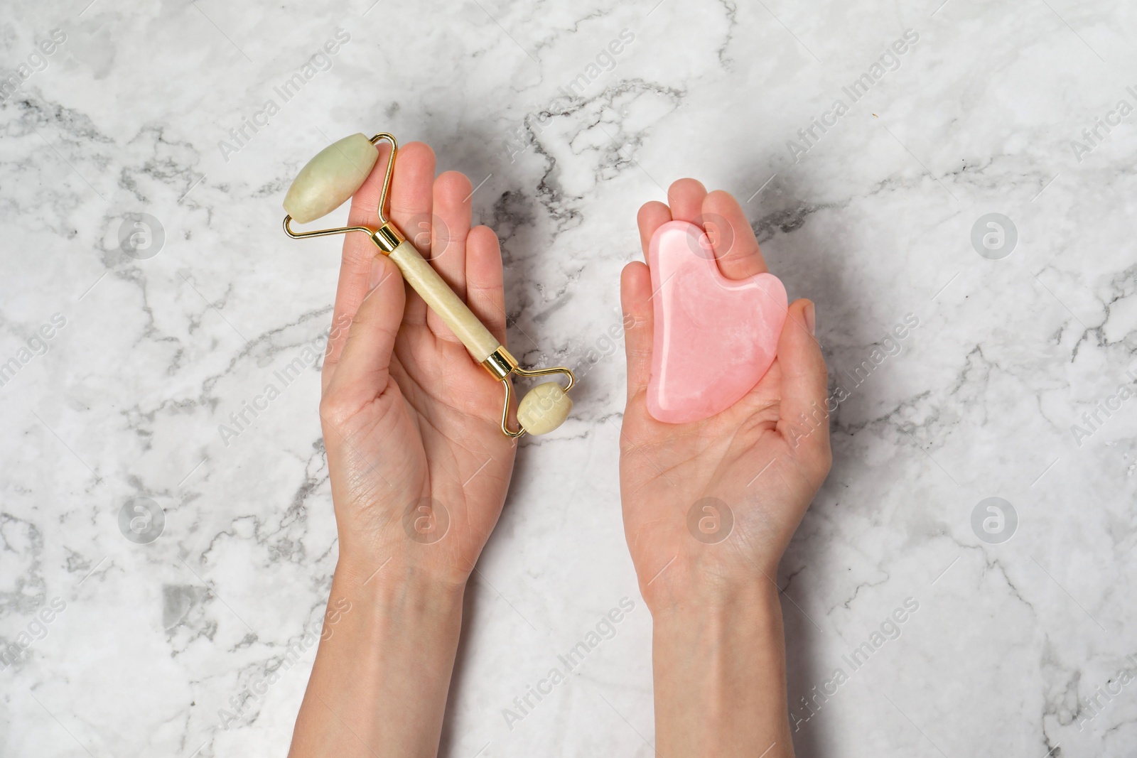 Photo of Woman with face roller and gua sha tool on white marble background, top view