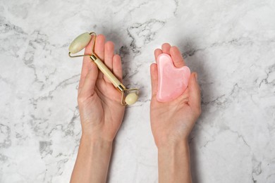 Photo of Woman with face roller and gua sha tool on white marble background, top view