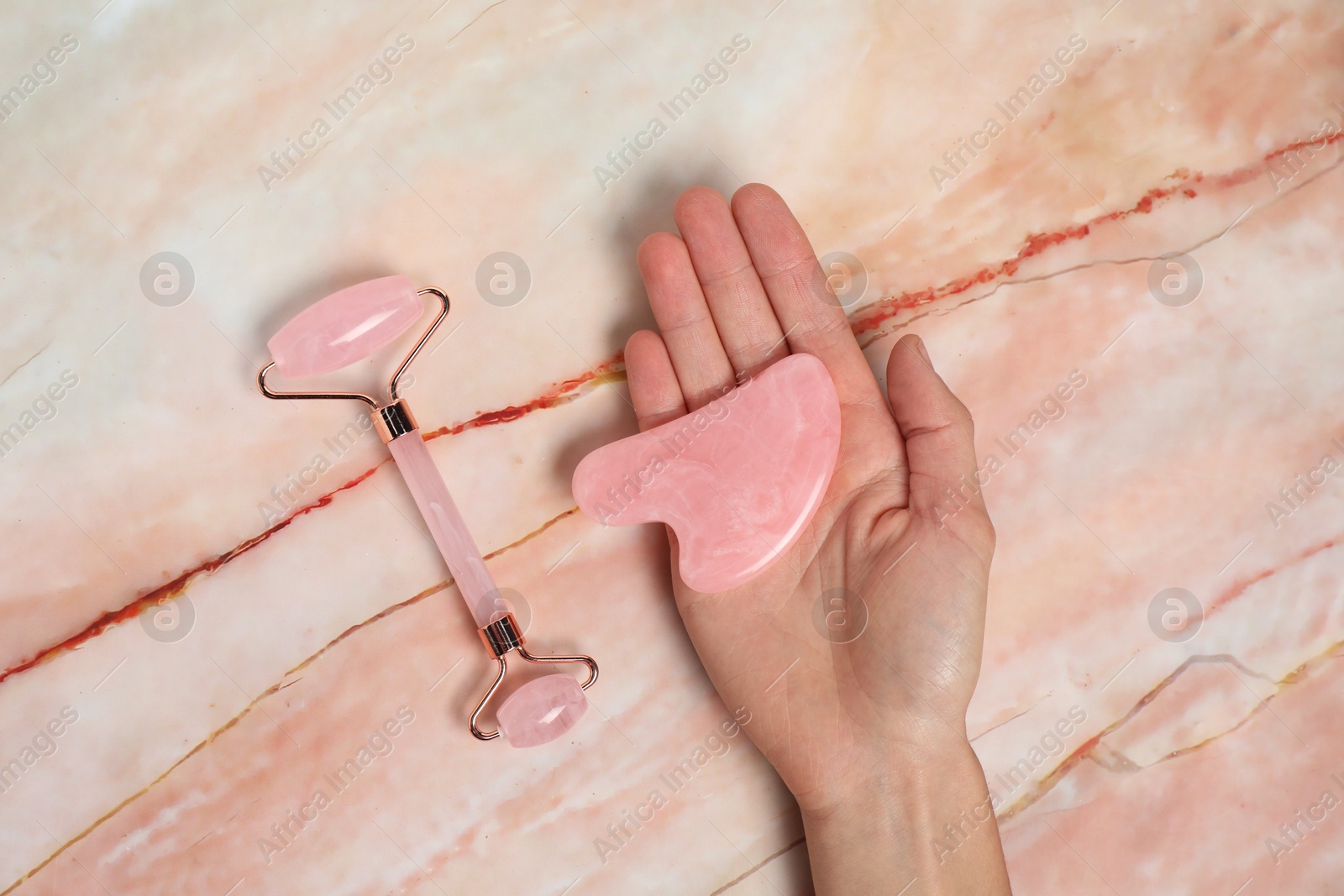 Photo of Woman with face roller and gua sha tool on pink marble background, top view