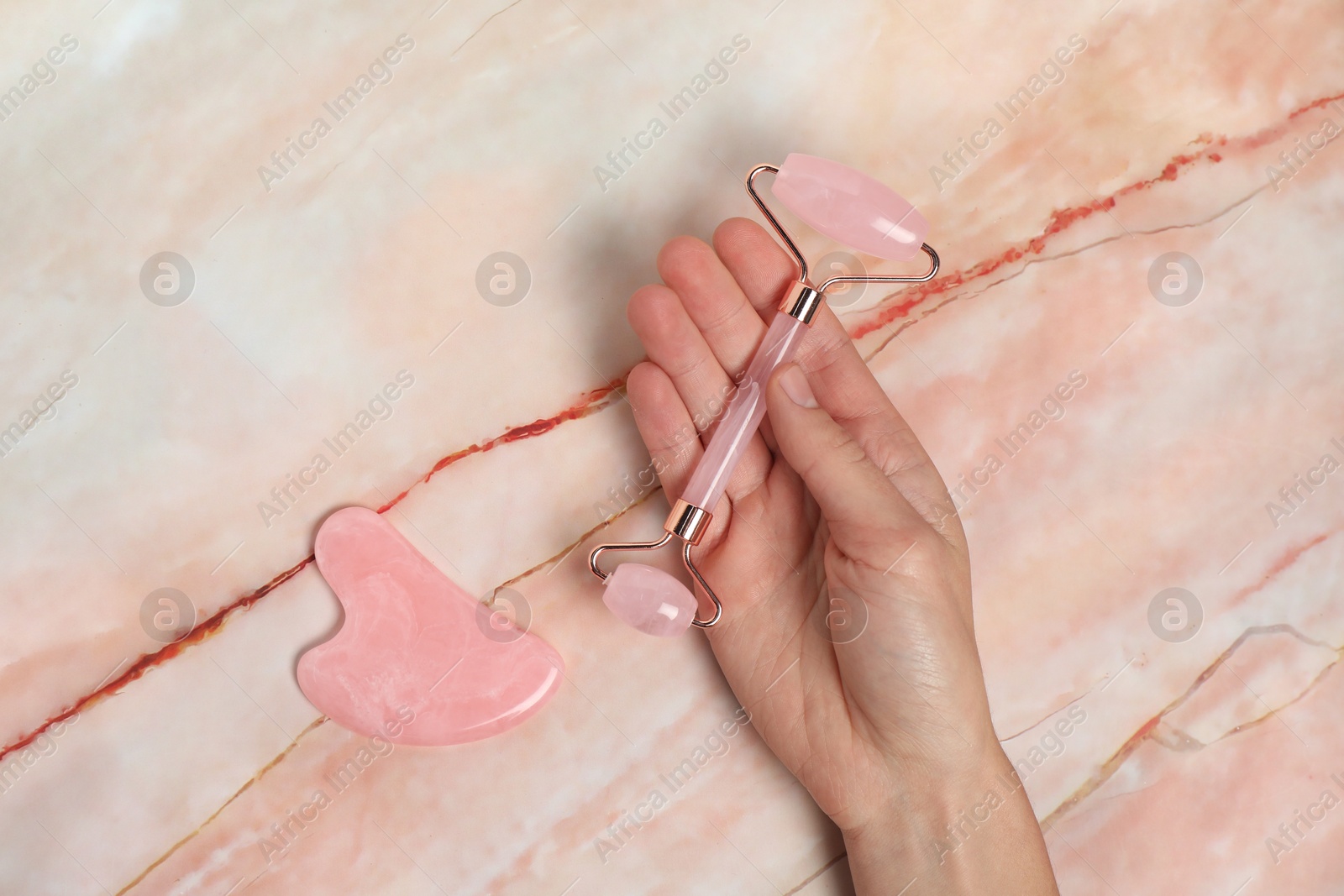 Photo of Woman with face roller and gua sha tool on pink marble background, top view