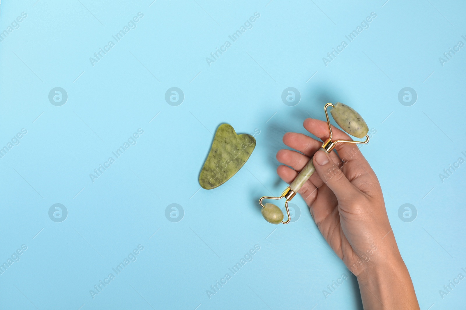 Photo of Woman with face roller and gua sha tool on light blue background, top view. Space for text