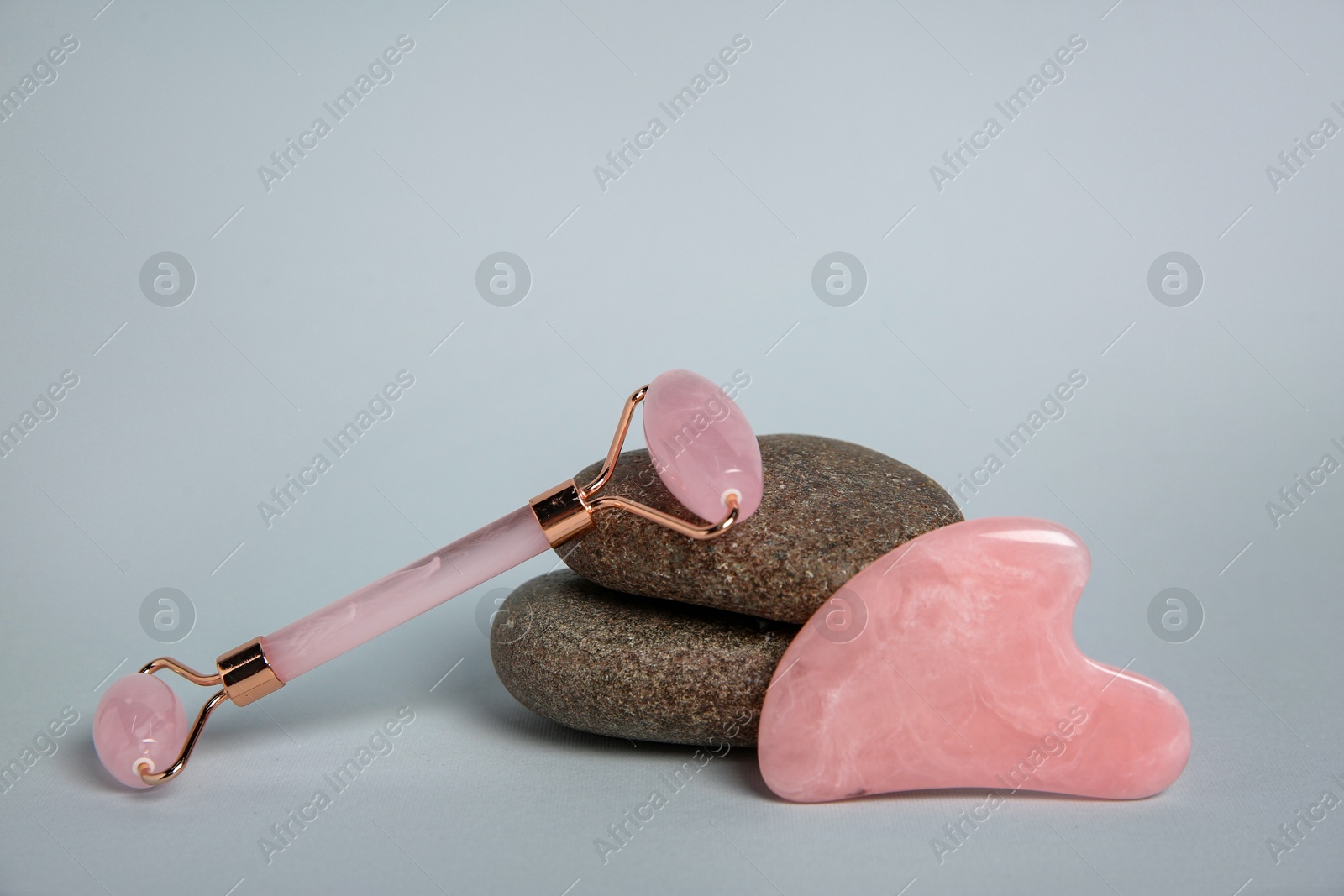 Photo of Face roller, gua sha tool and stones on light grey background