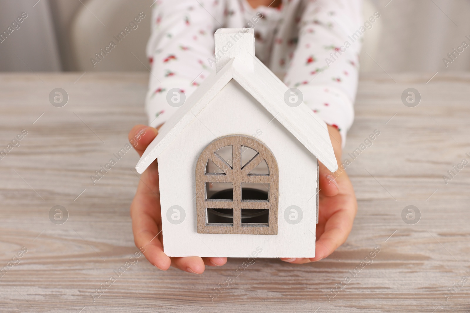 Photo of Adoption. Little girl with house figure at wooden table, closeup