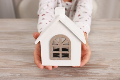 Photo of Adoption. Little girl with house figure at wooden table, closeup