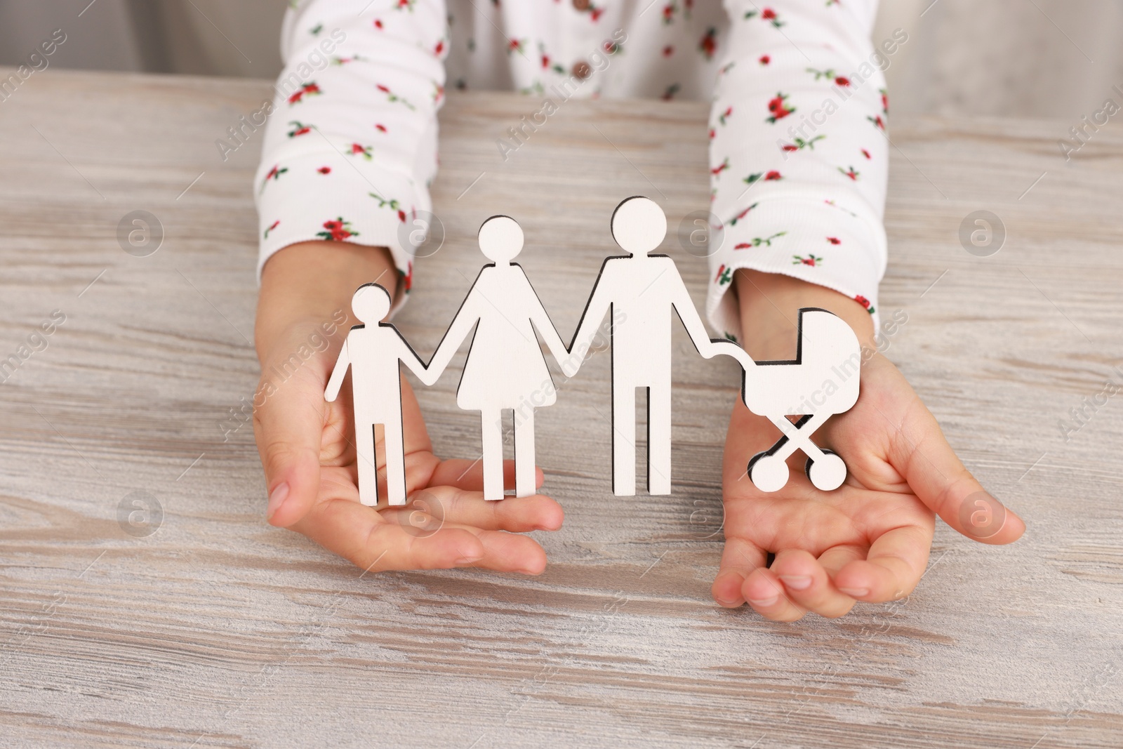 Photo of Adoption. Little girl with figures of family at wooden table, closeup