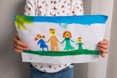 Photo of Adoption. Little girl holding drawing of family indoors, closeup