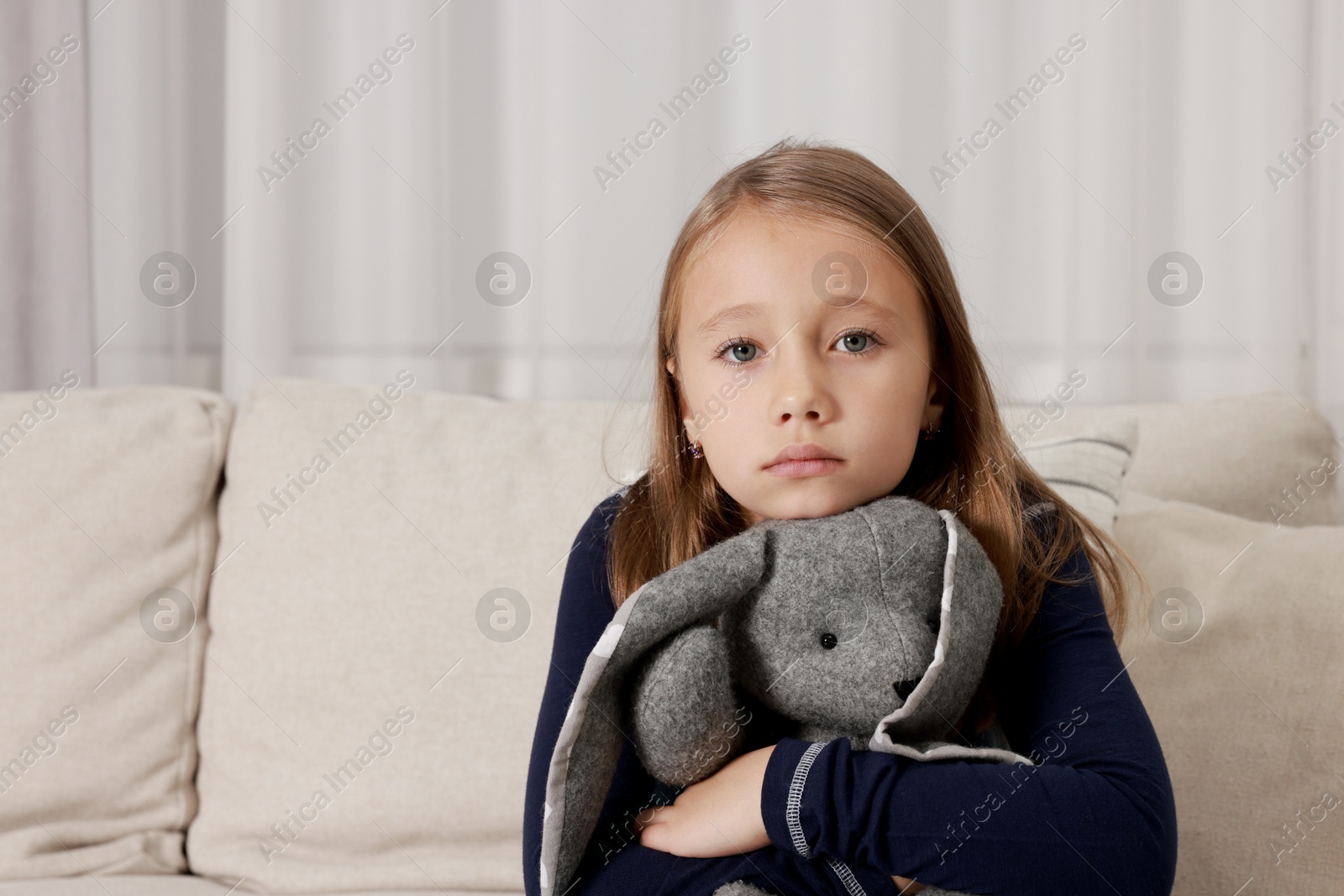 Photo of Autism concept. Lonely little girl with toy bunny on sofa at home