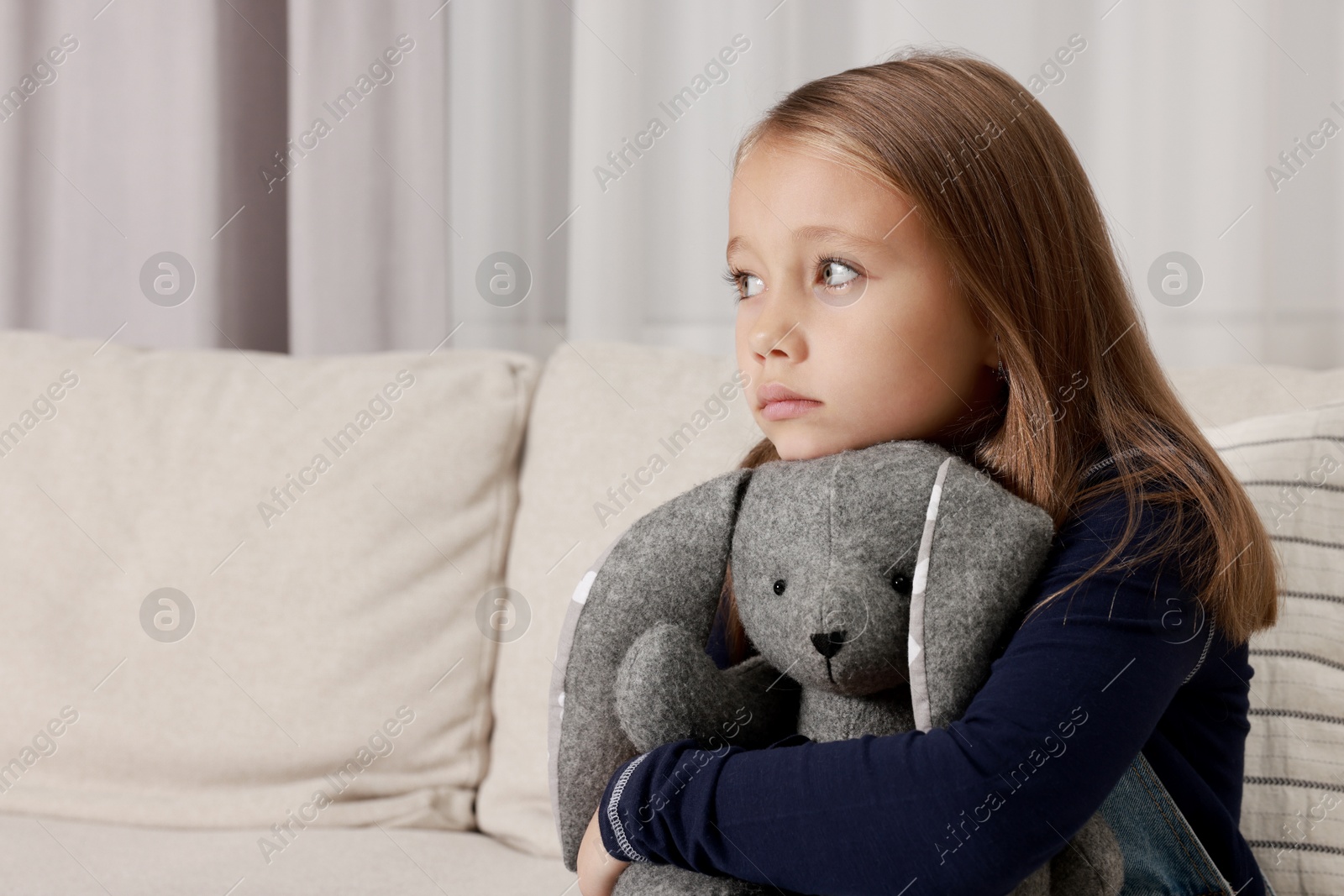 Photo of Autism concept. Lonely little girl with toy bunny on sofa at home