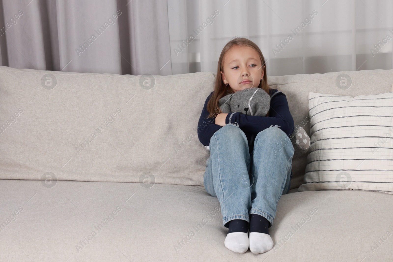 Photo of Autism concept. Lonely little girl with toy bunny on sofa at home