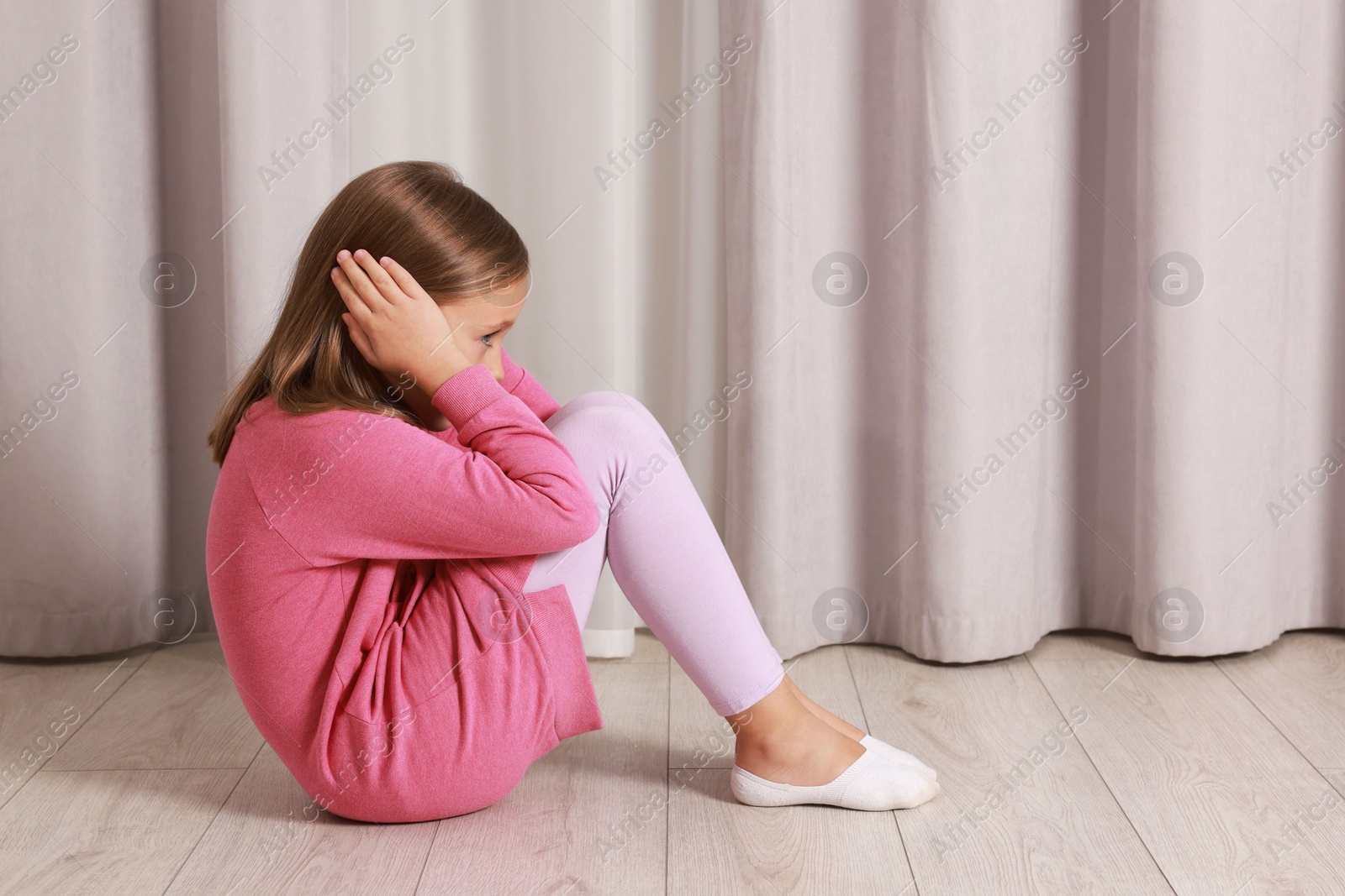 Photo of Autism concept. Scared little girl covering her ears on floor at home