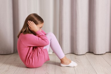 Photo of Autism concept. Scared little girl covering her ears on floor at home