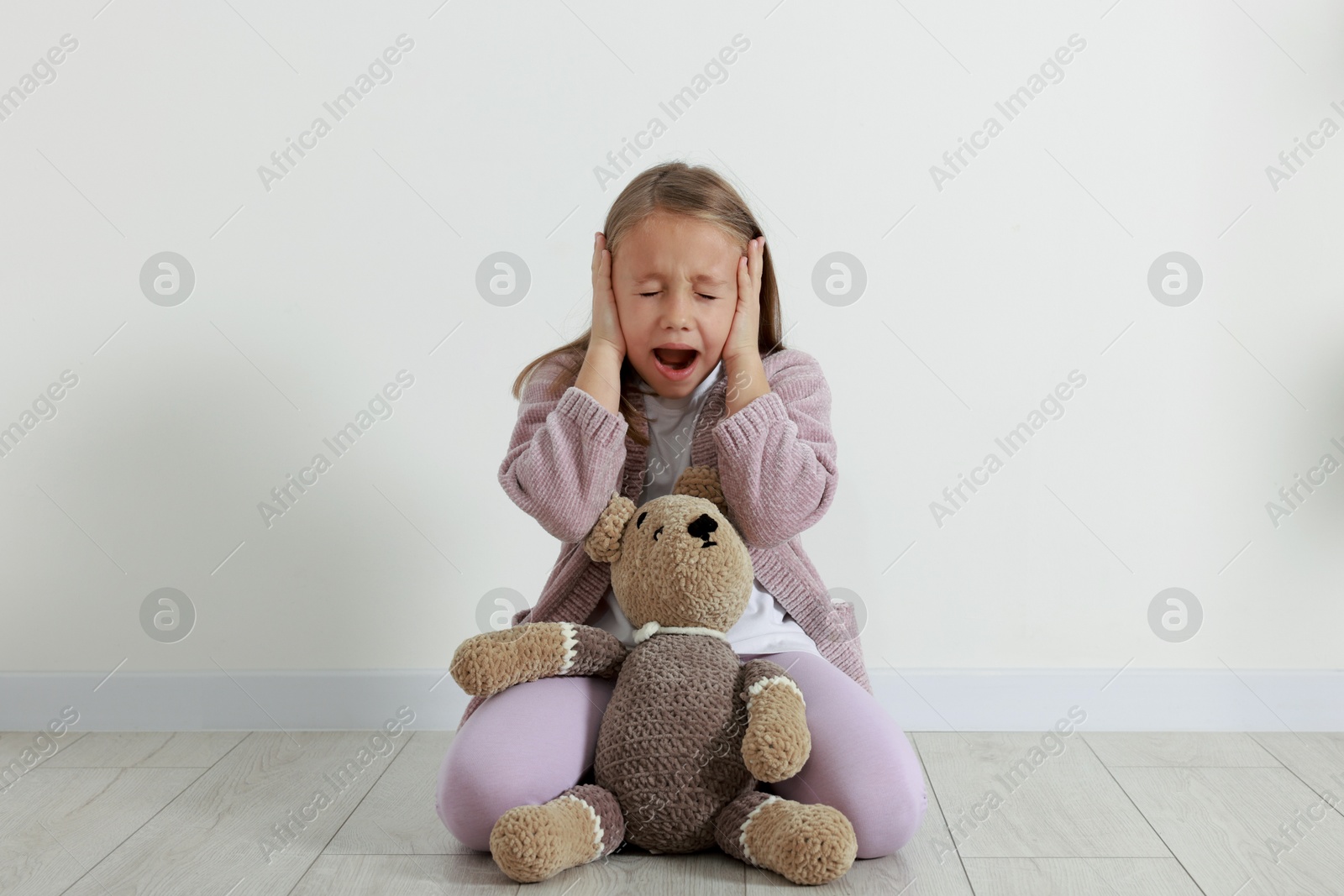 Photo of Autism concept. Scared little girl covering her ears on floor at home