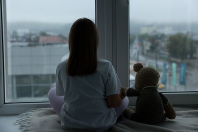 Photo of Autism concept. Lonely little girl near window at home