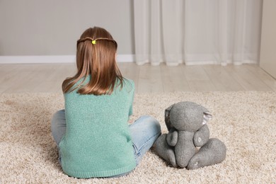 Photo of Autism concept. Lonely little girl with toy bunny on floor at home, back view