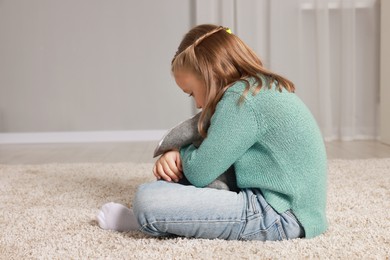 Photo of Autism concept. Lonely little girl with toy bunny on floor at home