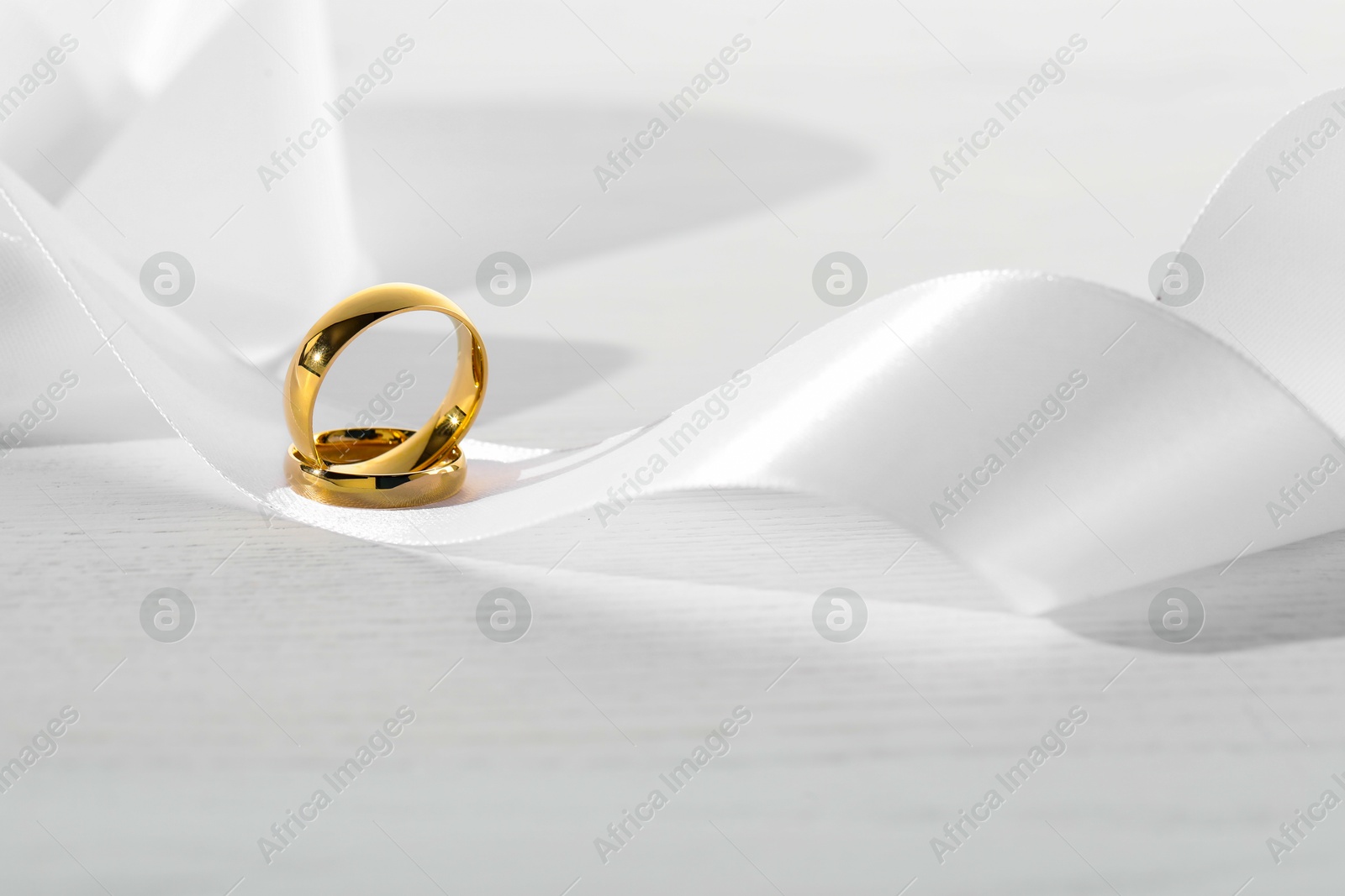 Photo of Beautiful golden wedding rings and white ribbon on light wooden background