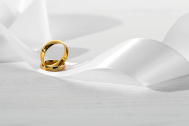 Beautiful golden wedding rings and white ribbon on light wooden background