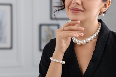 Photo of Young woman wearing elegant pearl jewelry indoors, closeup. Space for text