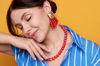 Young woman wearing stylish earrings and necklace on orange background, closeup