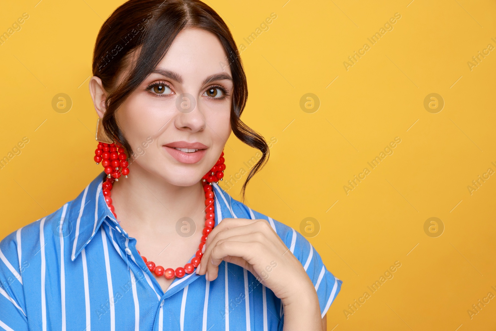 Photo of Young woman wearing stylish earrings and necklace on orange background. Space for text