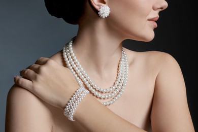 Photo of Woman wearing elegant pearl jewelry on dark grey background, closeup