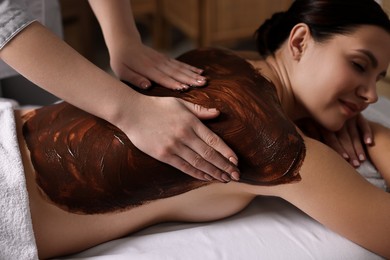 Woman undergoing chocolate body wrap treatment in spa salon