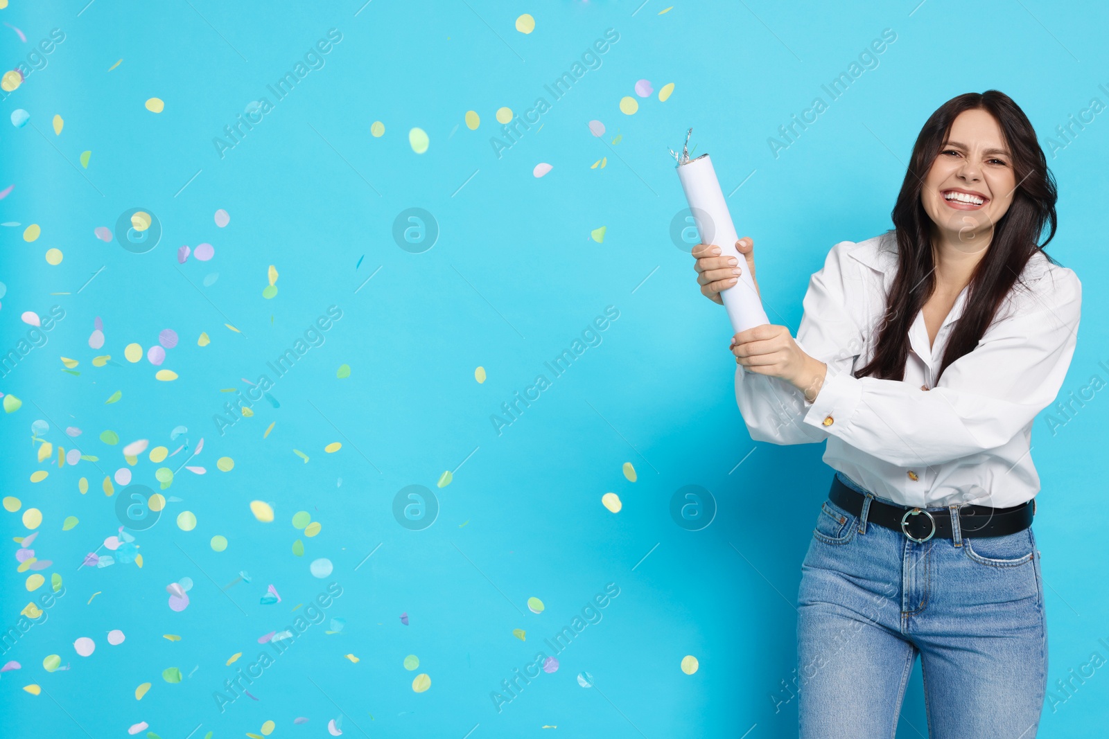 Photo of Happy woman blowing up confetti popper on light blue background, space for text. Surprise party