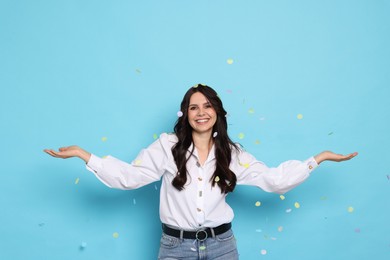 Happy woman under falling confetti on light blue background. Surprise party