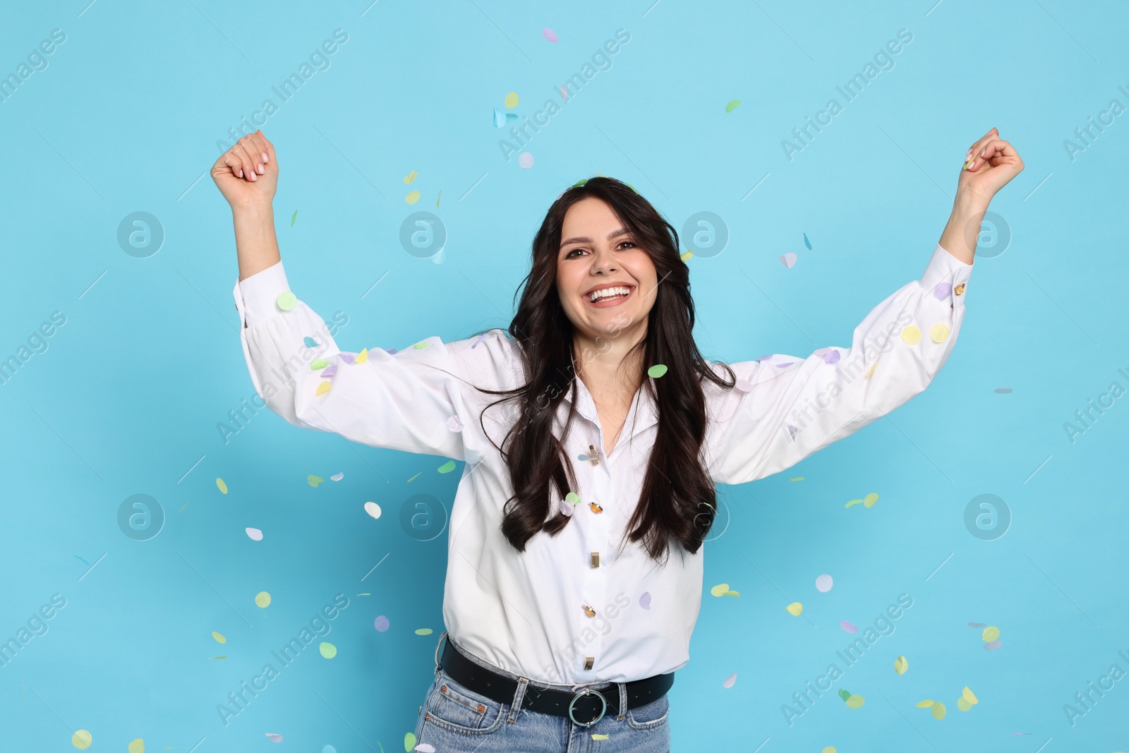 Photo of Happy woman under falling confetti on light blue background. Surprise party