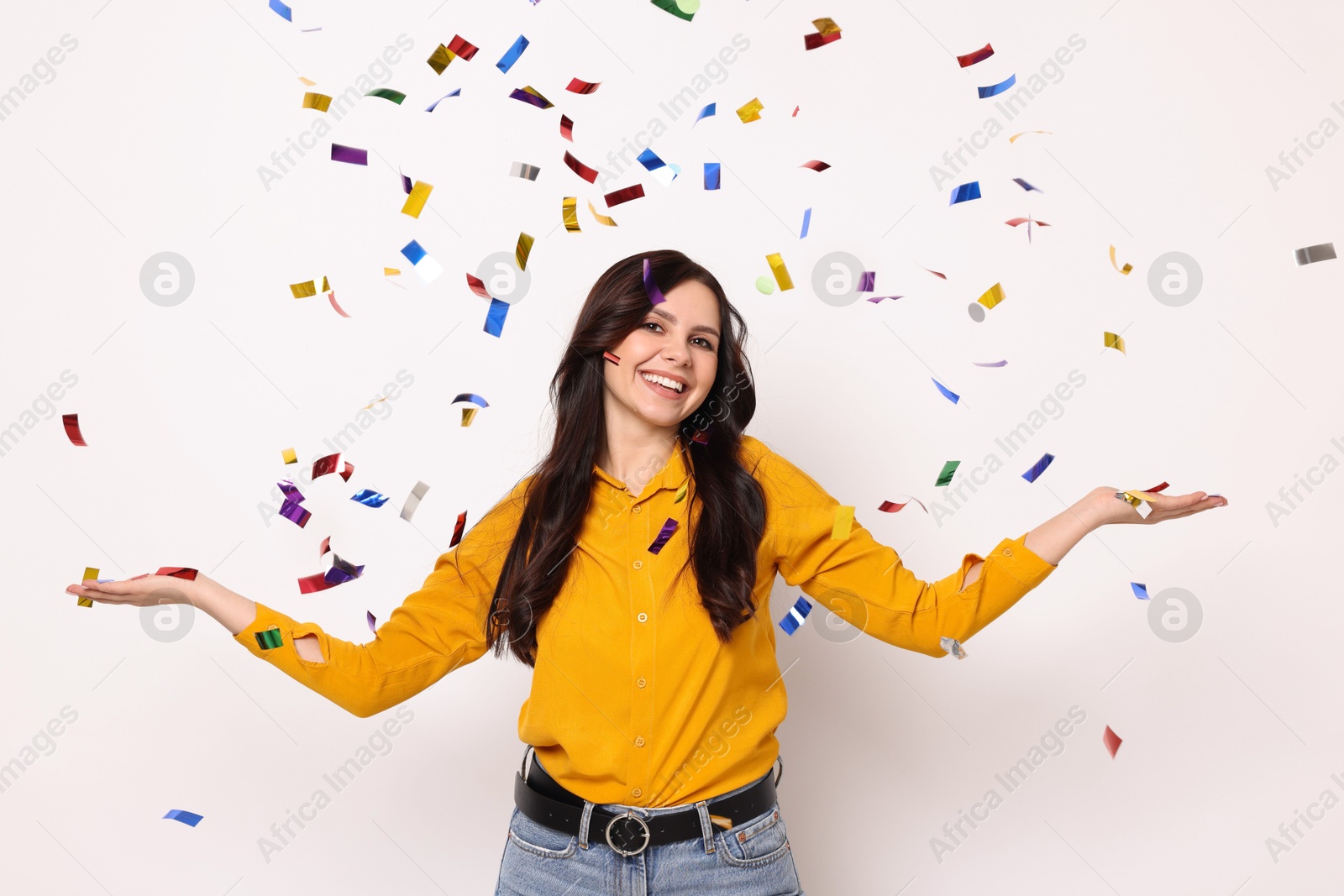 Photo of Happy woman under falling confetti on white background. Surprise party