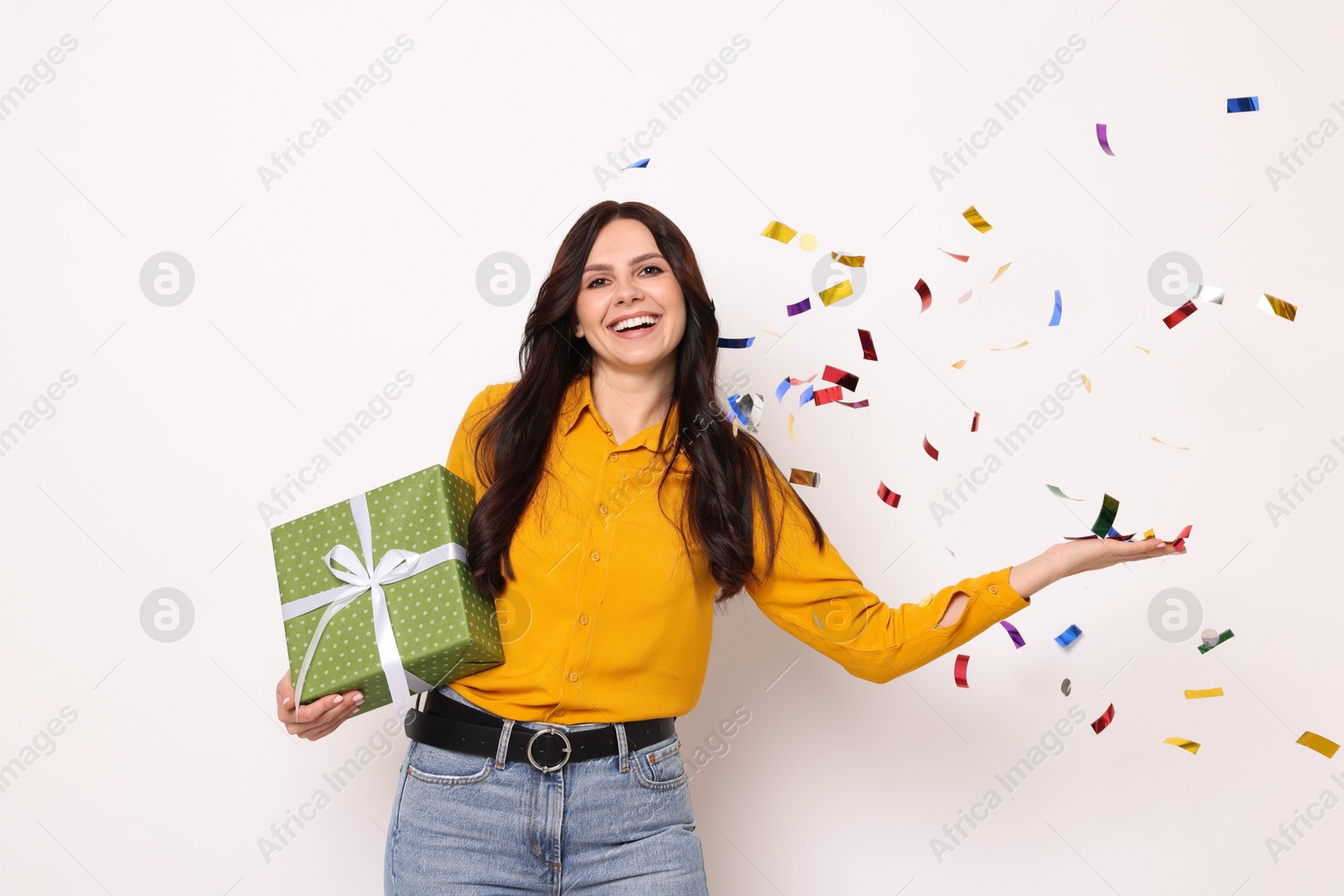 Photo of Happy woman with gift box and flying confetti on white background. Surprise party