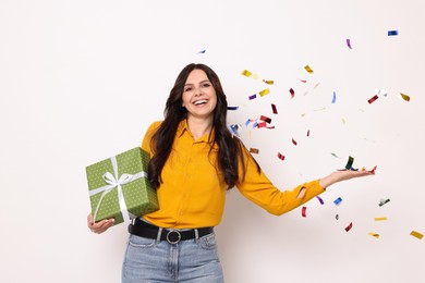 Happy woman with gift box and flying confetti on white background. Surprise party