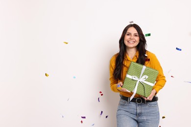 Photo of Happy woman with gift box and falling confetti on white background, space for text. Surprise party